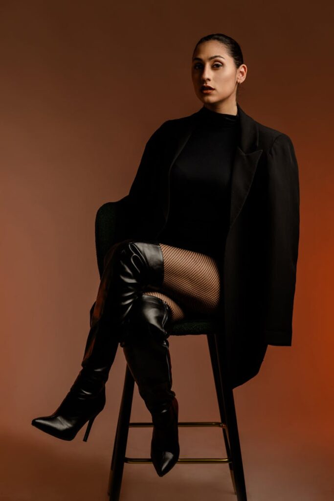 Elegant woman posing in a chic black outfit on a stool, exuding confidence.