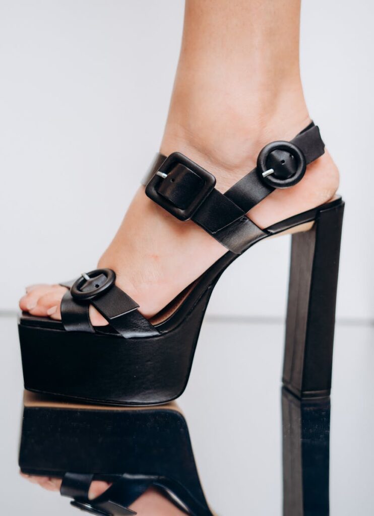Close-up of a black platform high heel shoe on a reflective surface, highlighting modern fashion.