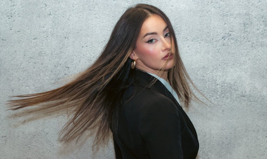 Stylish woman in a black blazer with flowing hair, showcasing elegance against a textured background.