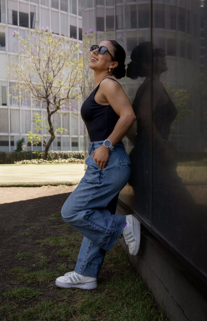 A woman poses confidently against a reflective wall in Mexico City, wearing sunglasses and a casual outfit.