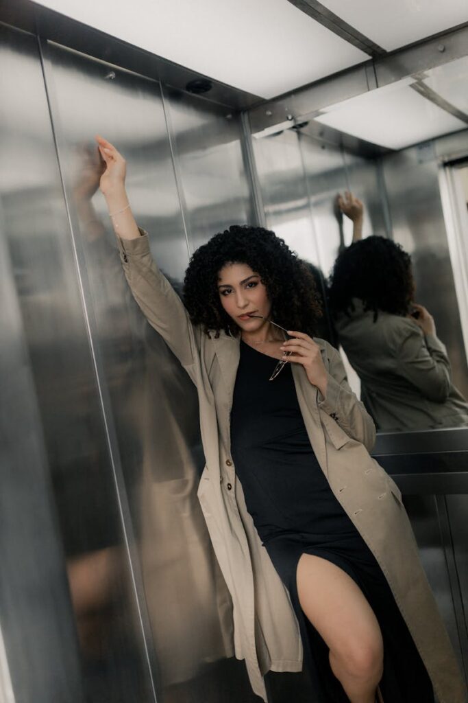 Elegant woman poses confidently in a metallic elevator, showcasing urban fashion.