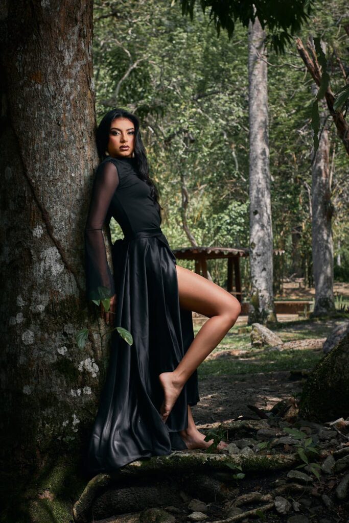 Graceful woman in black dress leaning against tree in a serene Venezuelan forest.