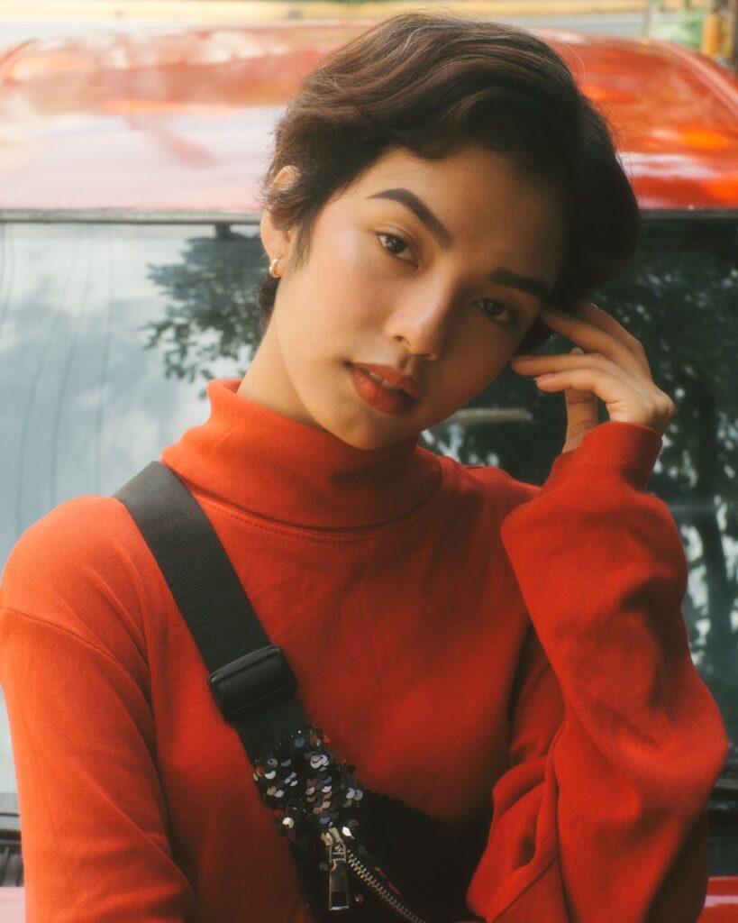 Portrait of a woman in a red turtleneck posing outdoors with a car in the background.