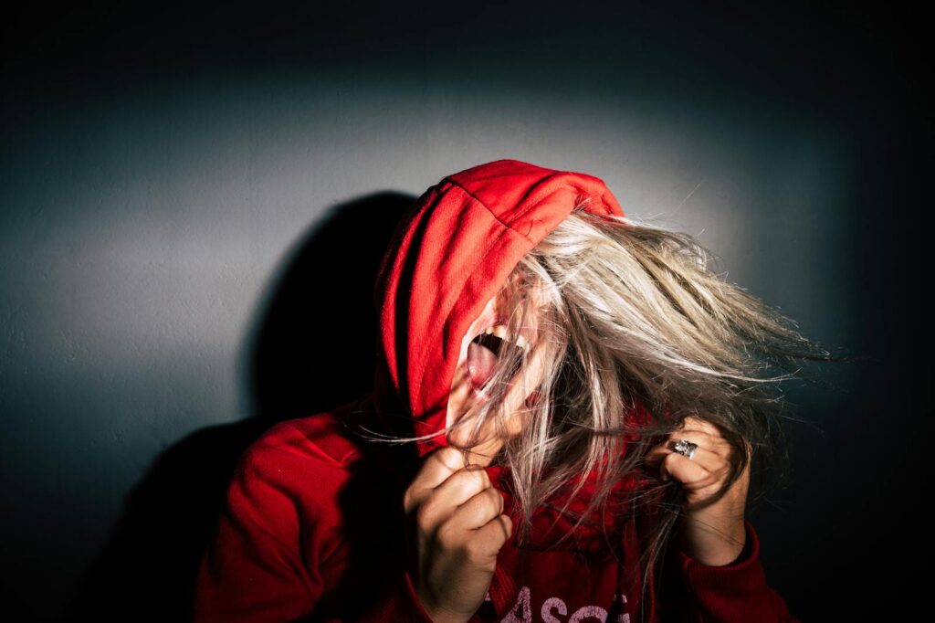 A teenager in a red hoodie screams with hair flying, conveying intense emotion.
