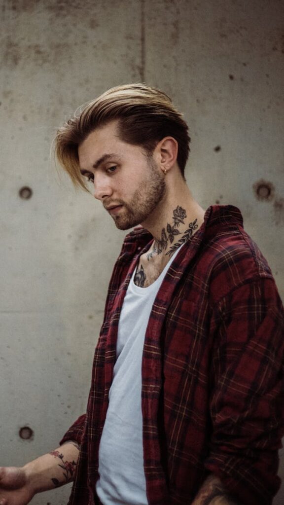 Stylish young man with tattoos wearing a plaid shirt, looking pensive.