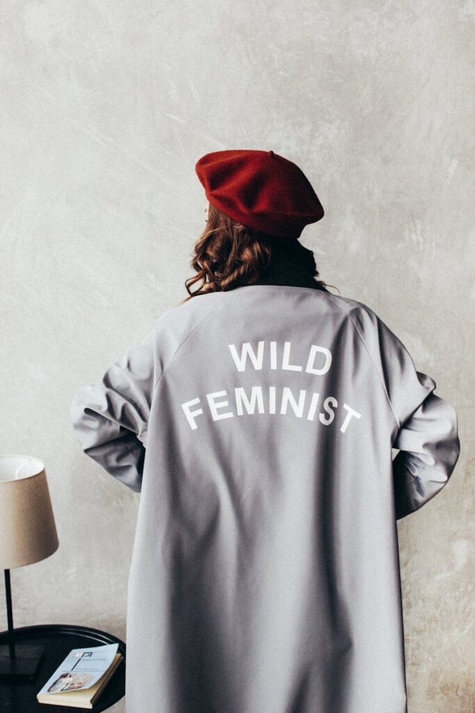 Woman in a red beret with 'Wild Feminist' coat in a cozy room setting.