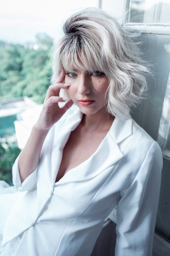 Fashionable woman with blonde hairstyle posing by a sunlit window.