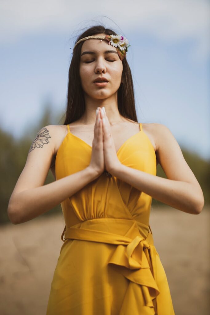 A young woman meditating outdoors in a yellow dress, embracing peace and relaxation.