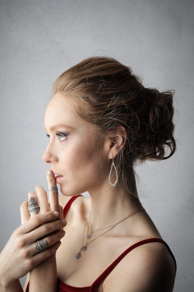 Profile of a woman in minimal jewelry and red top gazing thoughtfully.
