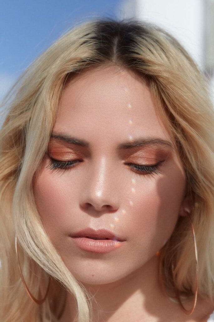Close-up portrait of a woman with blond hair and eye makeup in natural light.