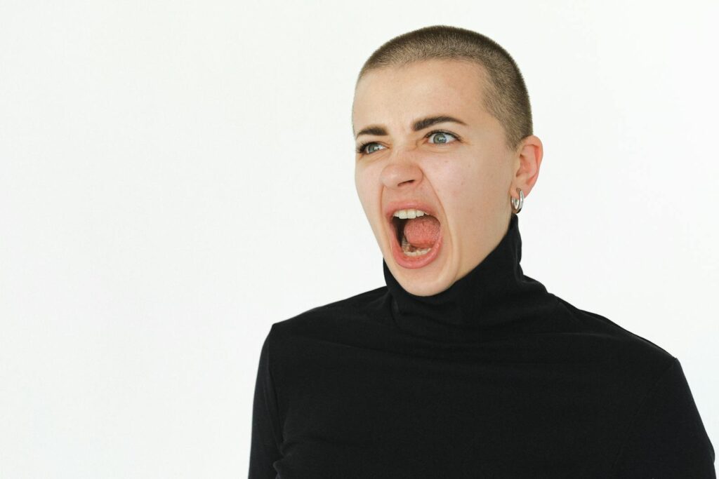 A woman yells expressively in a studio setting, wearing a black turtleneck.
