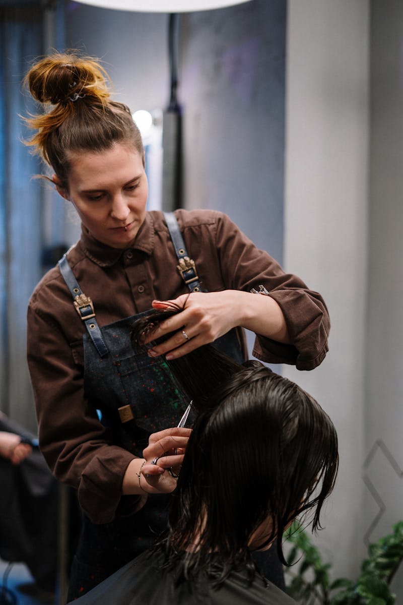 Focused female stylist cutting client’s wet hair in a modern salon setting.