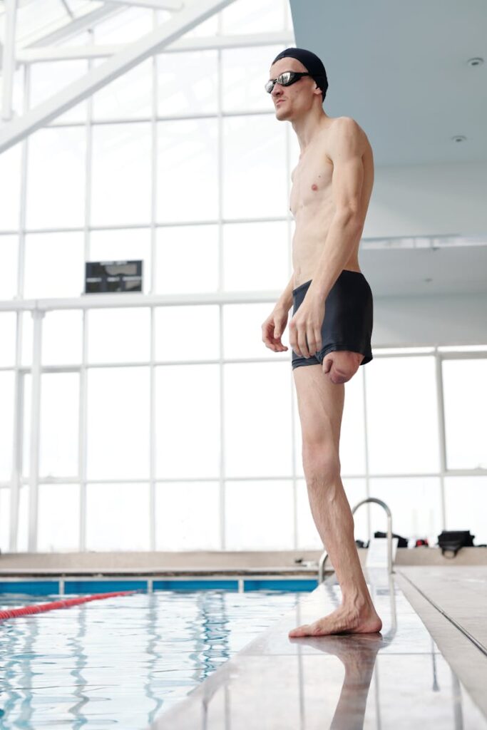 Amputee swimmer in swimwear standing by indoor pool, showcasing determination and fitness.