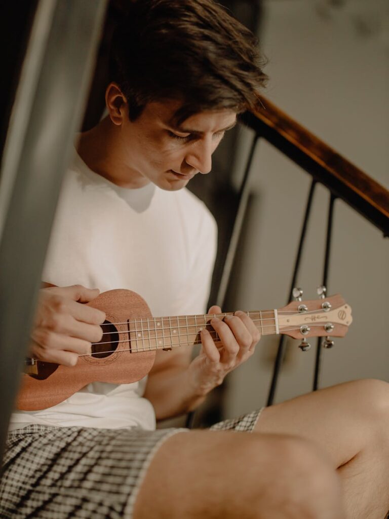 Relaxed man playing ukulele on staircase, enjoying a peaceful moment indoors.