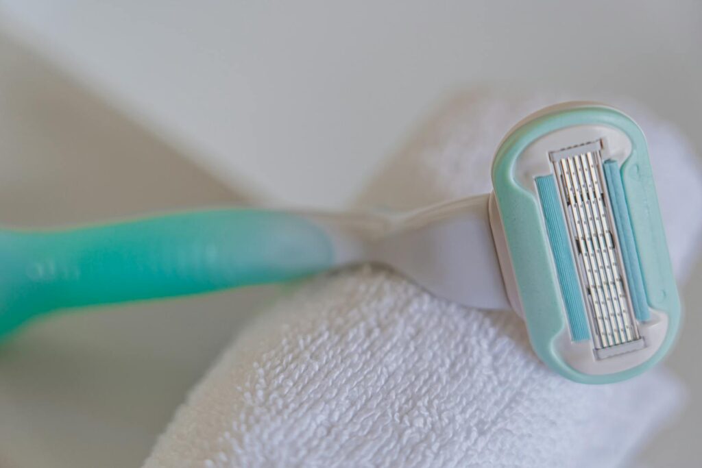 Disposable shaving razor with a teal handle on a white towel, perfect for personal care imagery.