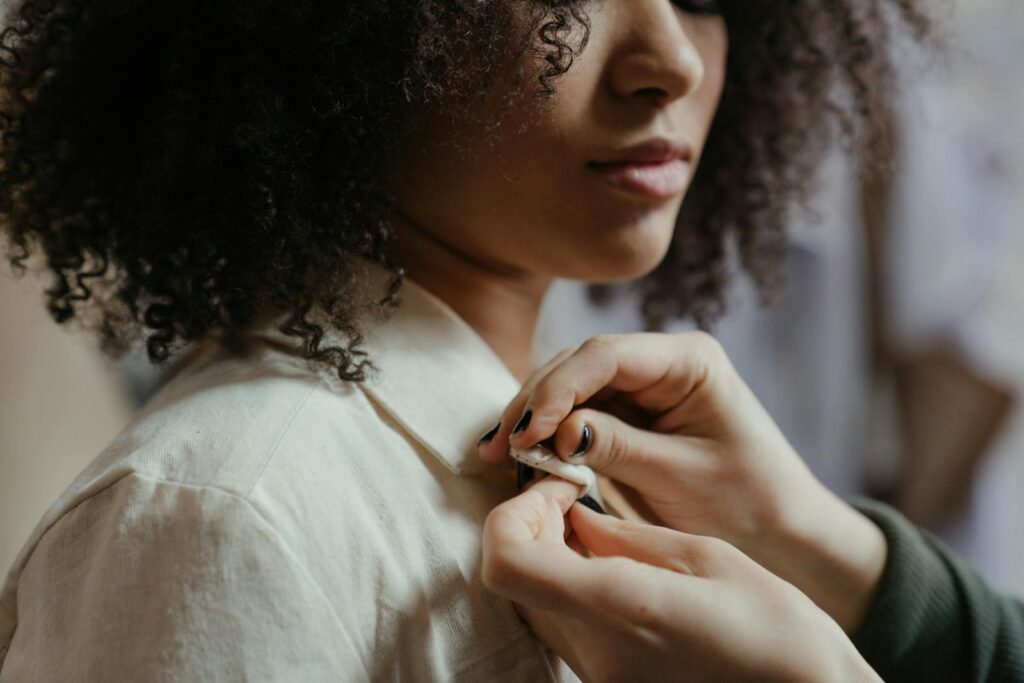 A detailed close-up of a tailor adjusting a shirt on a model with curly hair, showcasing precision.