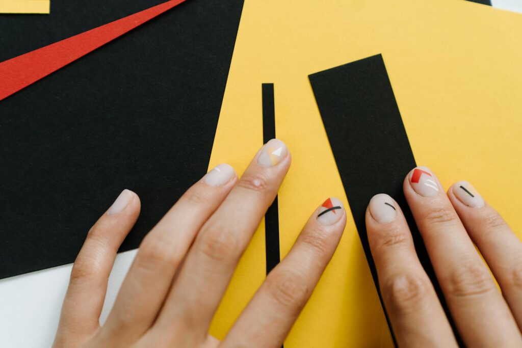 Close-up of modern nail art with geometric shapes on a yellow and black paper collage.