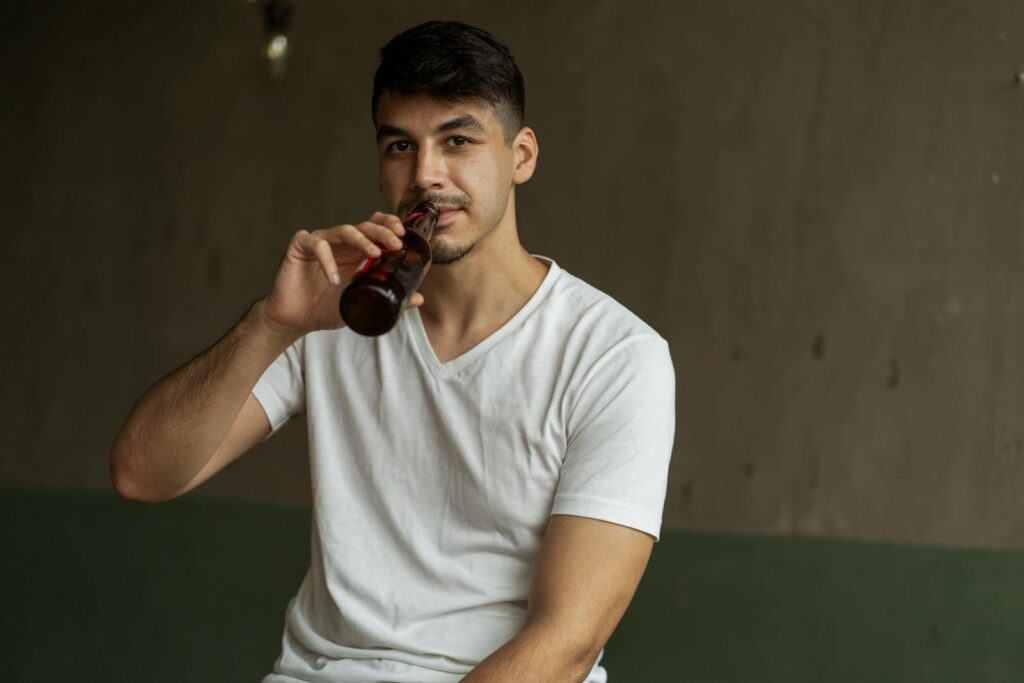 A man enjoys a drink indoors, holding a beer bottle in a casual setting.