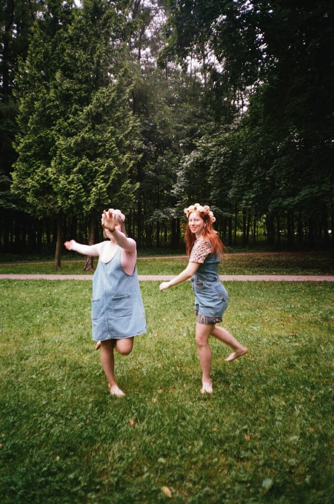 Two women joyfully playing barefoot in a green park with flower headbands.