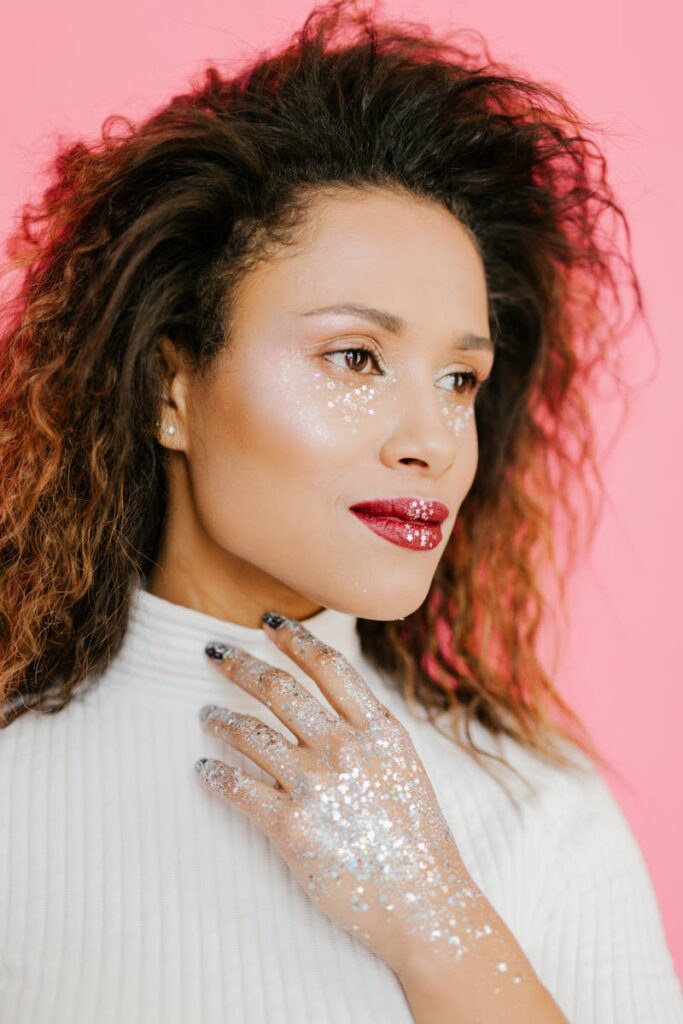 Fashion portrait of a woman with glitter makeup on a pink background, exuding elegance and style.