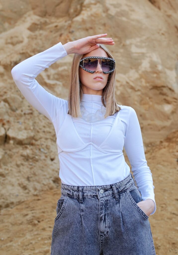 Trendy woman in sunglasses and casual outfit posing against a rocky backdrop.