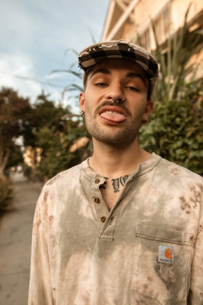 Casual portrait of a young man with tattoos and a tie-dye shirt, expressing a rebellious style.