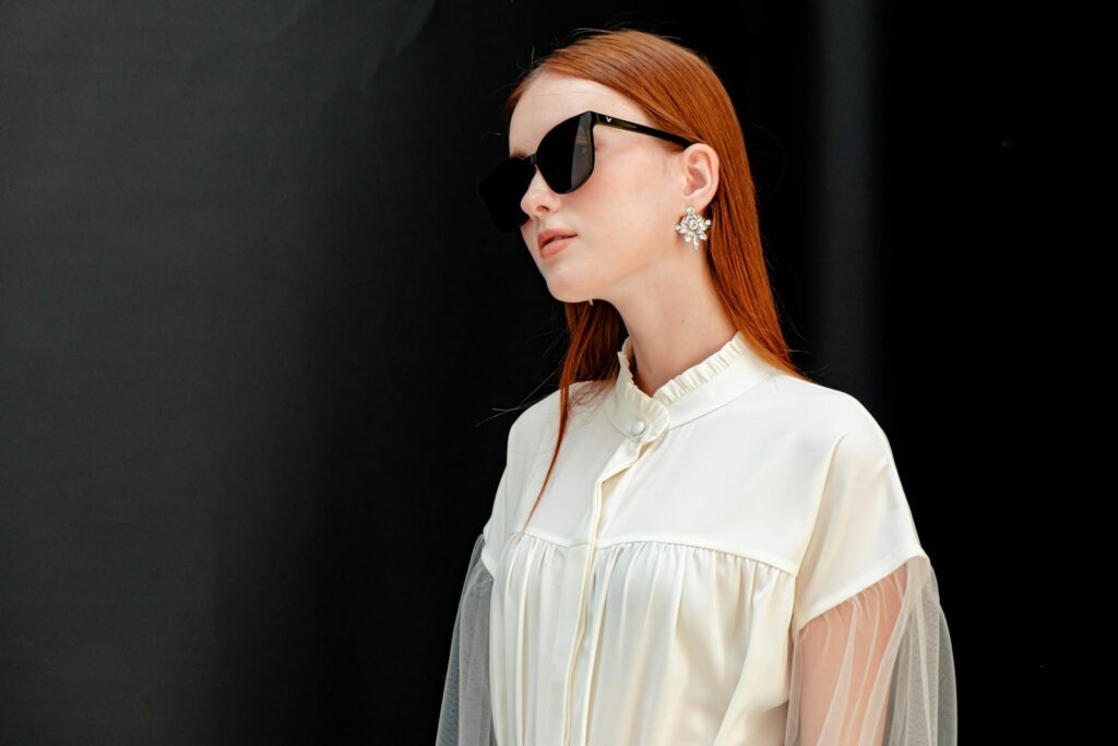 Fashion portrait of a stylish woman in sunglasses with elegant earrings and a chic white outfit.