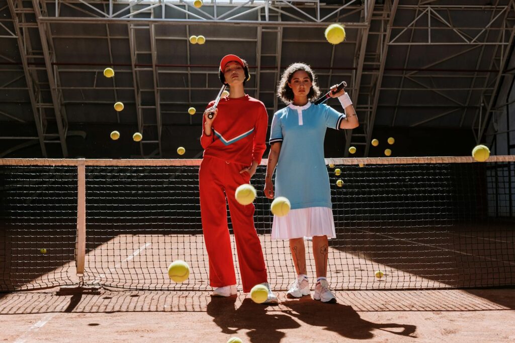 Energetic shot of two athletes posing with tennis rackets on a court, surrounded by bouncing tennis balls.