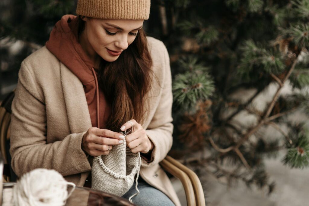 A woman enjoys knitting outdoors in a cozy autumn setting with warm clothing.