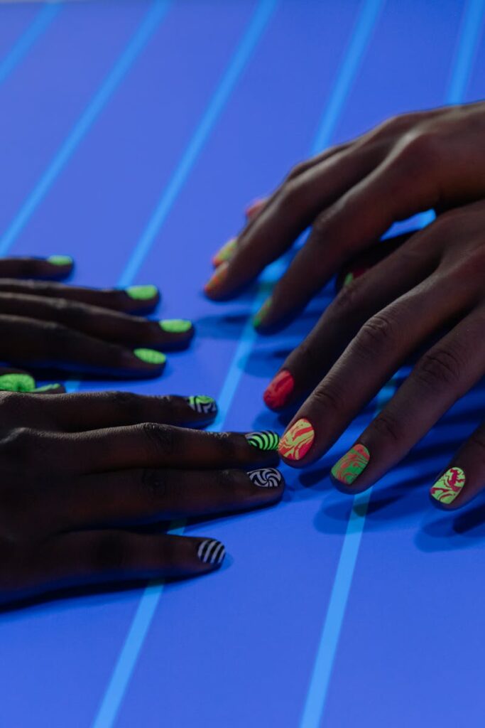 Creative nail art design with vibrant neon colors on hands under UV light, showcasing modern manicure styles.