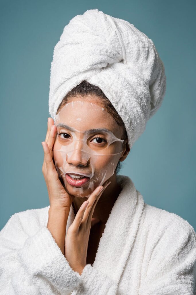 A woman in a white bathrobe applies a sheet mask, promoting skincare routine.