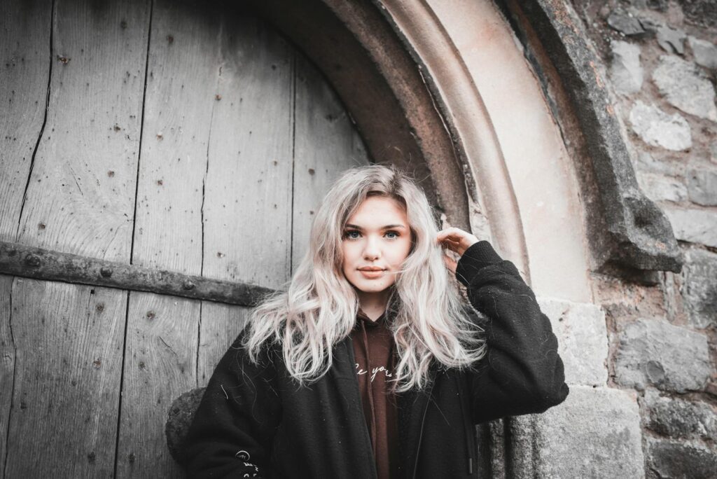 Portrait of a woman with blonde hair standing by an ancient stone and wooden arched door.