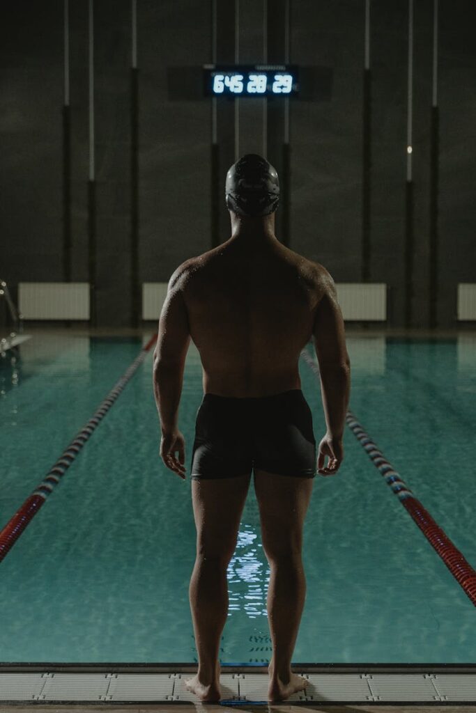 Back view of a swimmer in a dark swimming pool, getting ready for a dive. Perfect for fitness and sports themes.