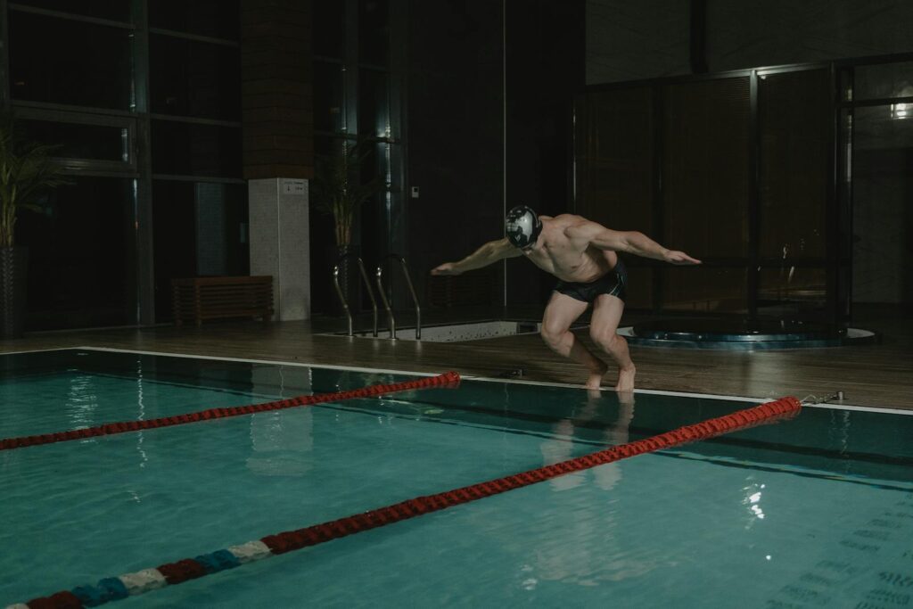 Athlete diving into an indoor swimming pool at night, showcasing fitness and energy.