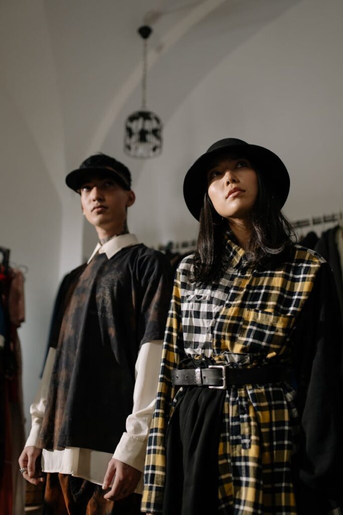 A fashionable man and woman in stylish outfits posing indoors with hats.