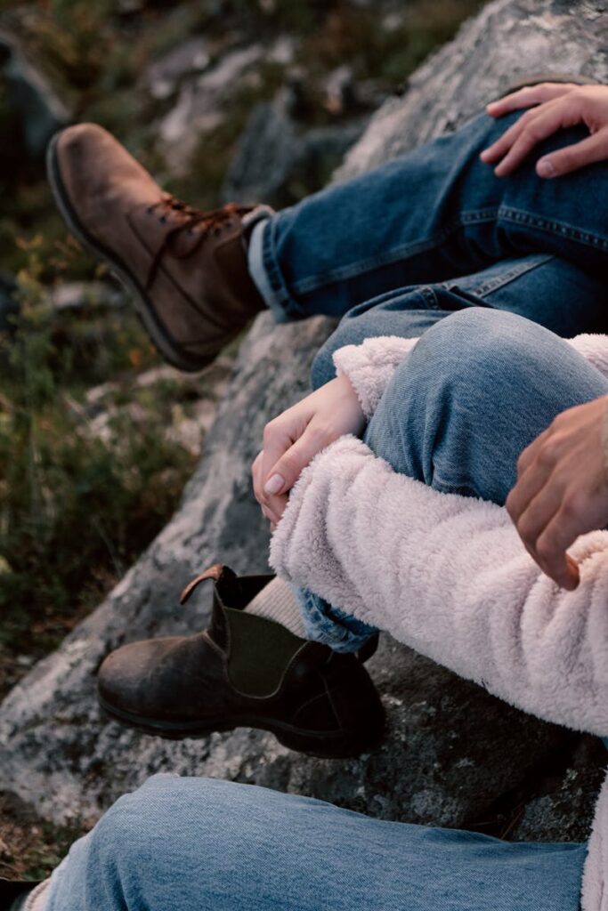 Close-up of two people relaxing outdoors on rocky terrain wearing casual attire and boots.