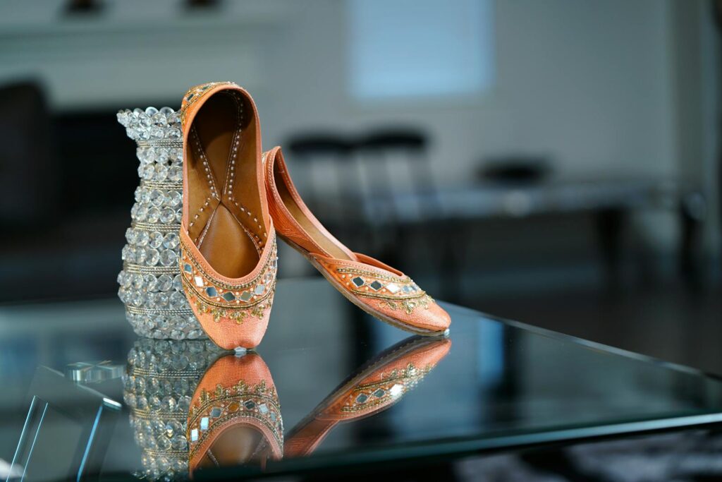 Elegant pink ballet flat shoes decorated with sparkling crystals and arranged on glass table near cut glass vase