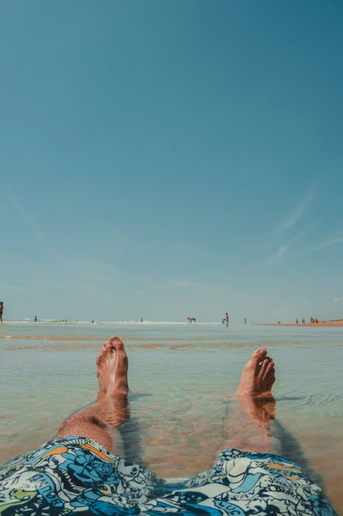 Person relaxing on a sunny beach with clear water and blue skies, embodying leisure and tranquility.