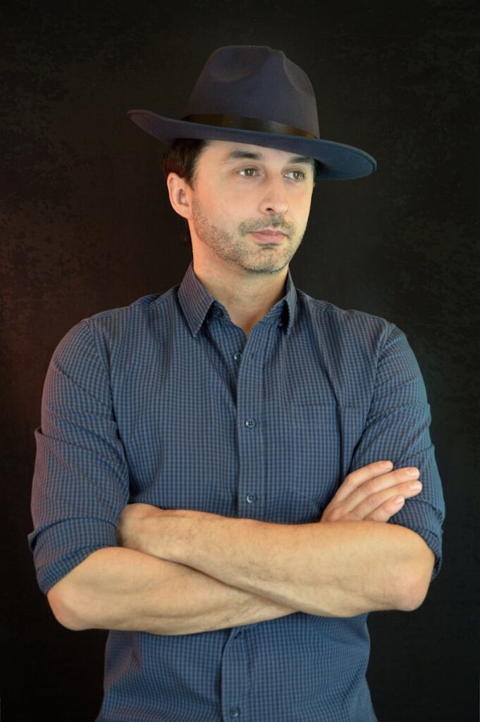 Confident gentleman in a hat with crossed arms against a dark backdrop. Studio shot.