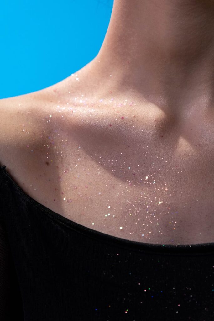 A close-up portrait of a woman's collarbone adorned with sparkling glitter.