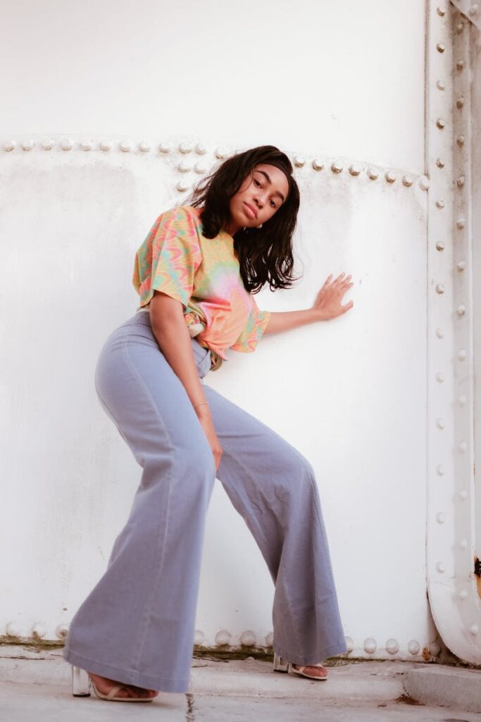 Young woman posing in trendy bell-bottom jeans and colorful top, showcasing modern fashion.