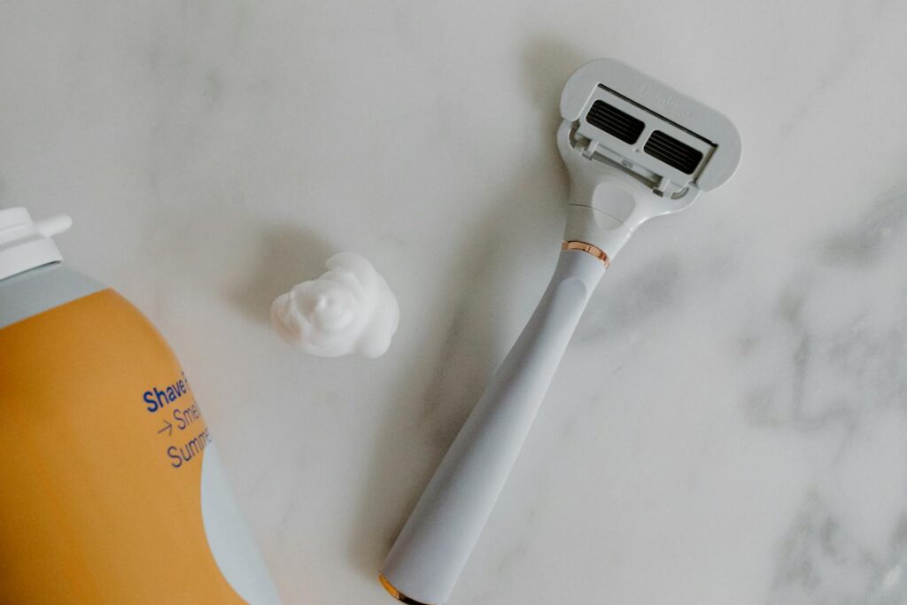Top view of a razor and shaving foam on a marble surface, perfect for grooming and lifestyle themes.