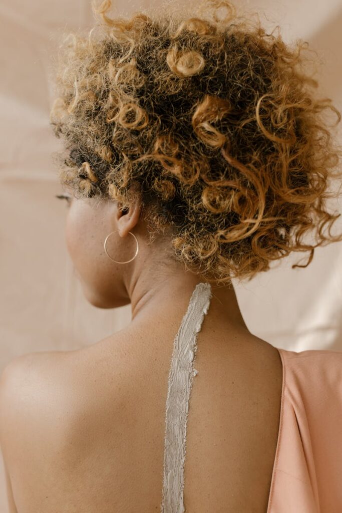 Artistic rear view of a woman with curly hair and a clay texture on her back, highlighting unique beauty.