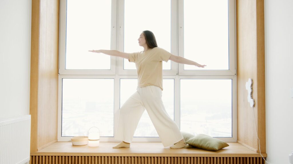 A woman balances in a yoga pose on a windowsill with natural light.