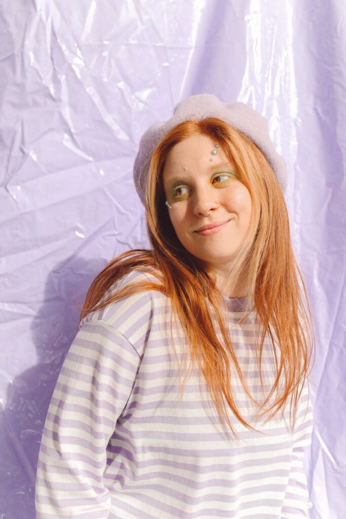 Teen girl with red hair and beret, smiling in studio with pastel backdrop.