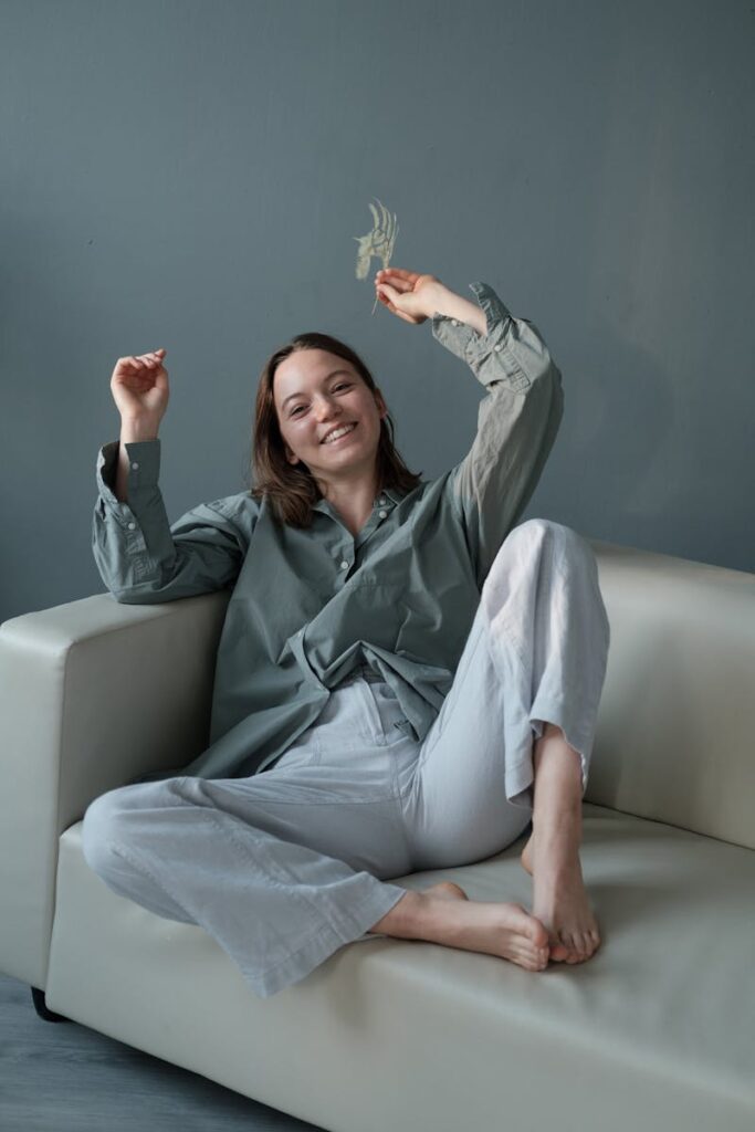 Smiling woman enjoying a relaxing moment on a couch with greenery indoors.