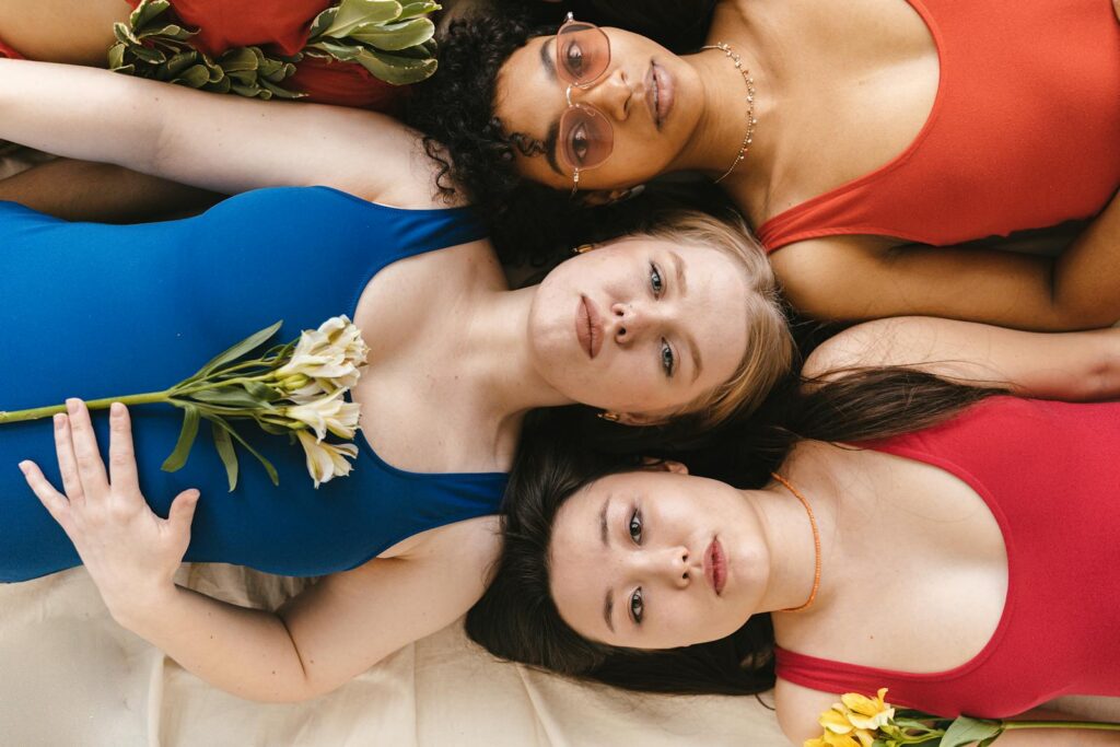 Top view of diverse women in colorful swimwear lying with flowers, highlighting beauty and diversity.