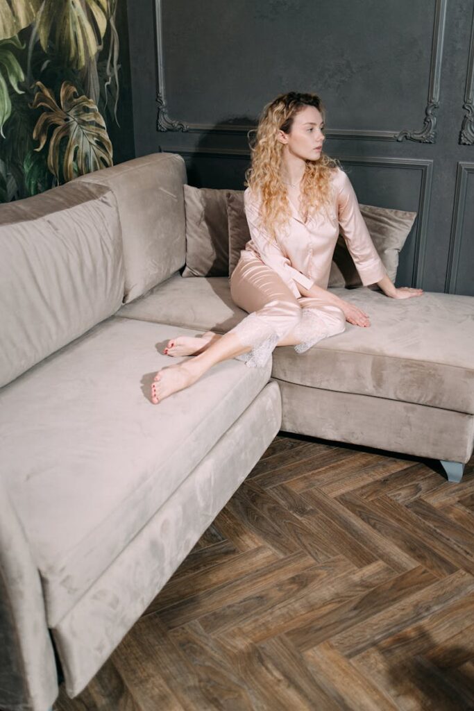 Elegant woman with curly hair in silk sleepwear lounging on a plush couch indoors.