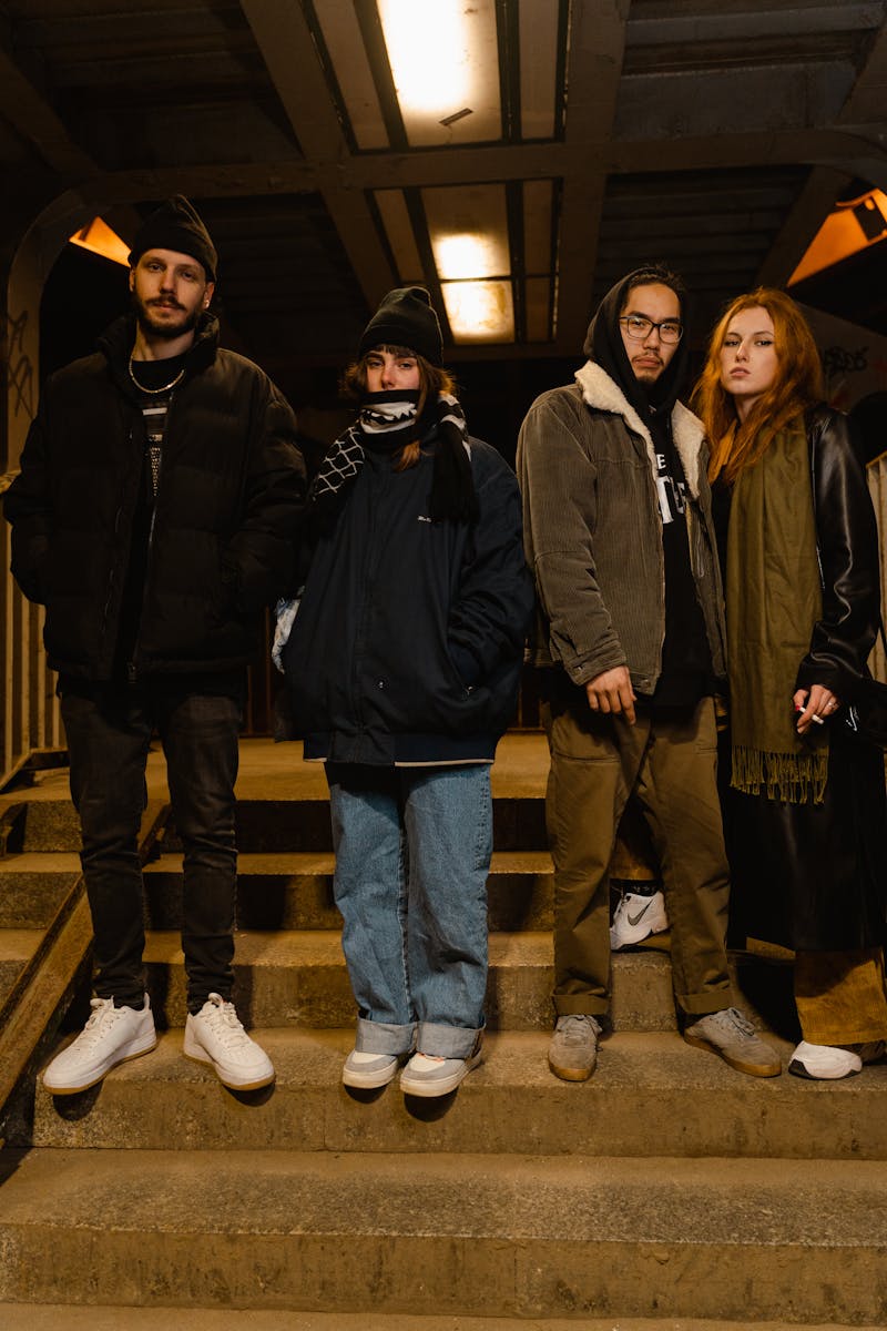 A diverse group of four friends standing together on stairs at night, showcasing modern winter fashion.