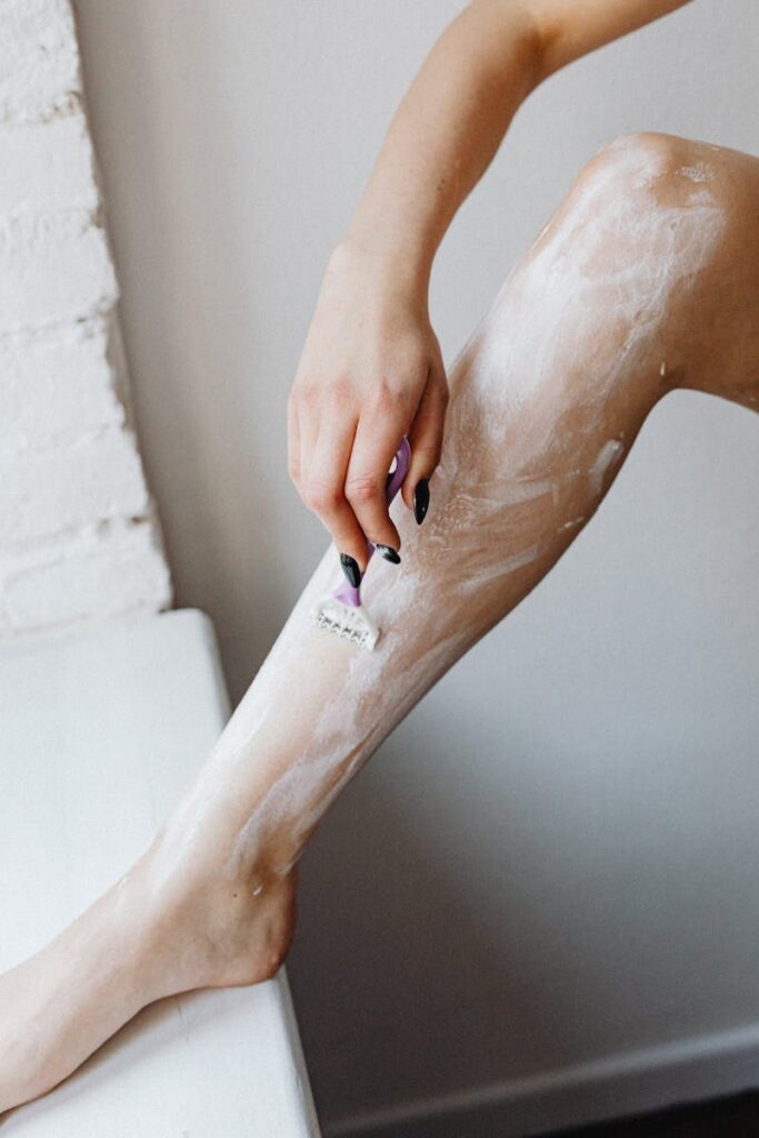 Woman shaving her leg with foam using a razor, showcasing personal grooming.